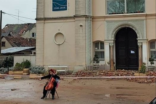 Sara Kolar svira violončelo ispred razrušene glazbene škole u Sisku