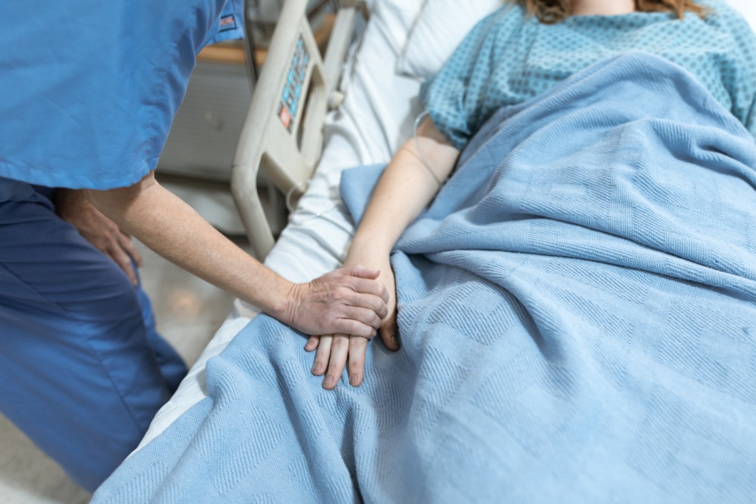 Pacijentica leži na krevetu, a medicinska sestra drži ju za ruku
